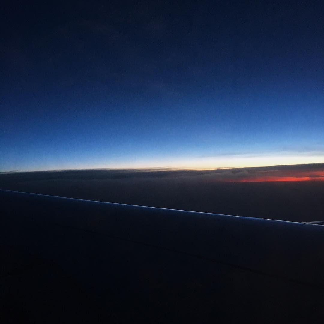 Blick aus Flugzeugfenster bei Morgenrot, Tragfläche sichtbar, schmaler leuchtender Streifen zwischen Wolken und tiefblauem Himmel. (KI-generiert)
